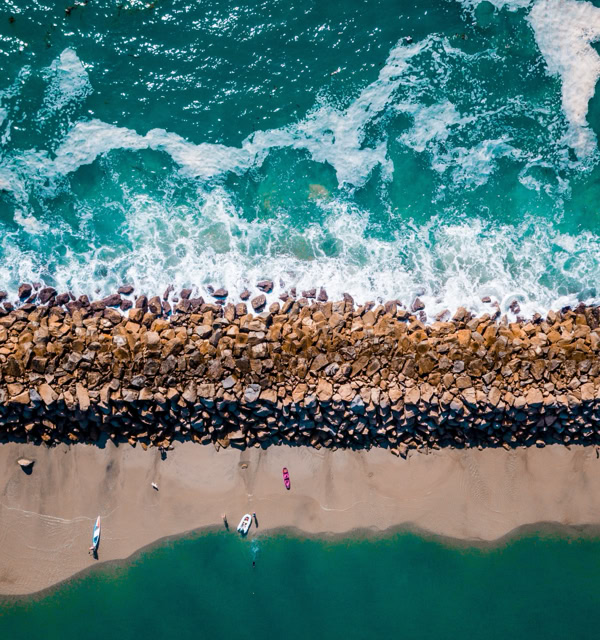 Aerial view of a beach with waves crashing against a rocky breakwater.