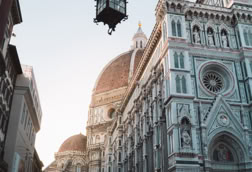 Street view of Florence Cathedral with its dome and intricate facade, under a clear sky.