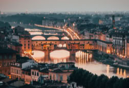 Aerial view of a cityscape at sunset with illuminated bridges over a river.
