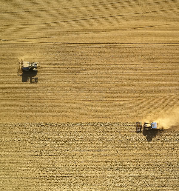 Aerial view of two tractors working in a large, golden wheat field.
